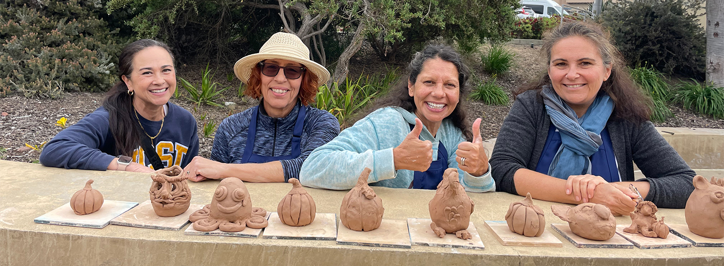 a line of shaped clay with four people smiling and sitting behind them 